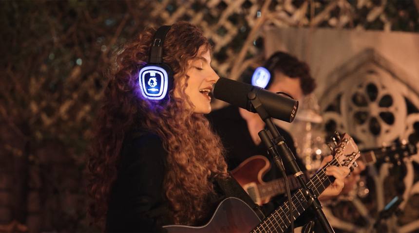 Curly-haired singer performing with an acoustic guitar in headphones