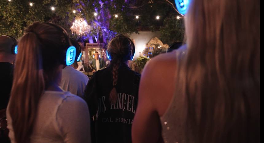 Crowd from behind facing the candlelit stage in glowing headphones